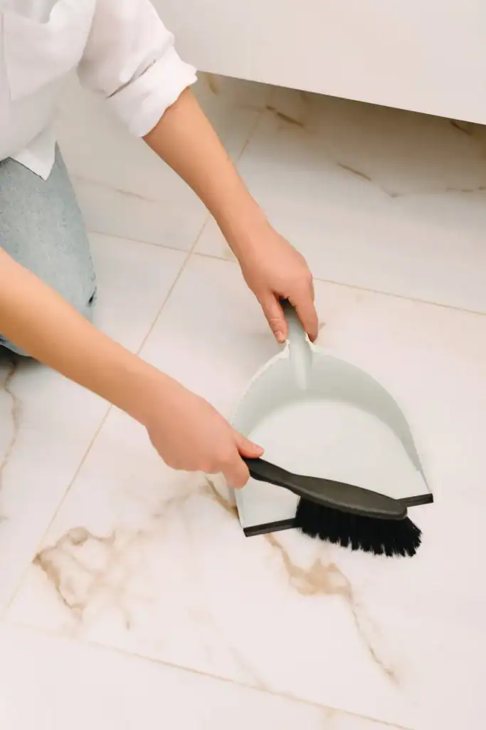 Sweeping a marble tile floor with a dustpan and hand brush before mopping with a diy floor cleaner