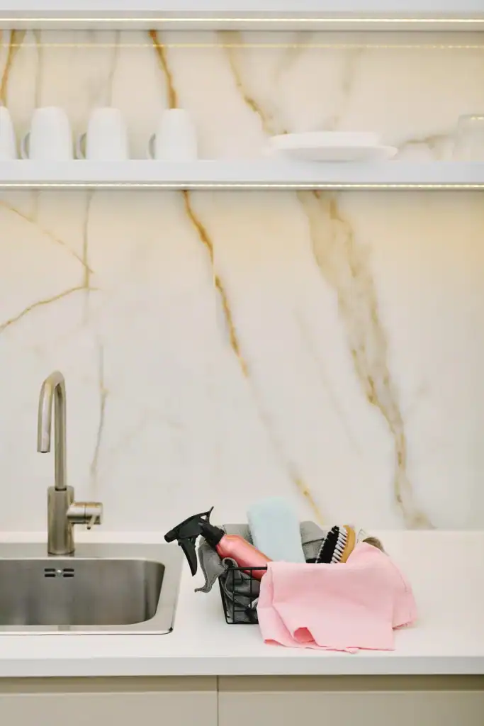 Homemade floor cleaner in a pink glass spray bottle beside folded microfiber cloths on a bright white marble counter
