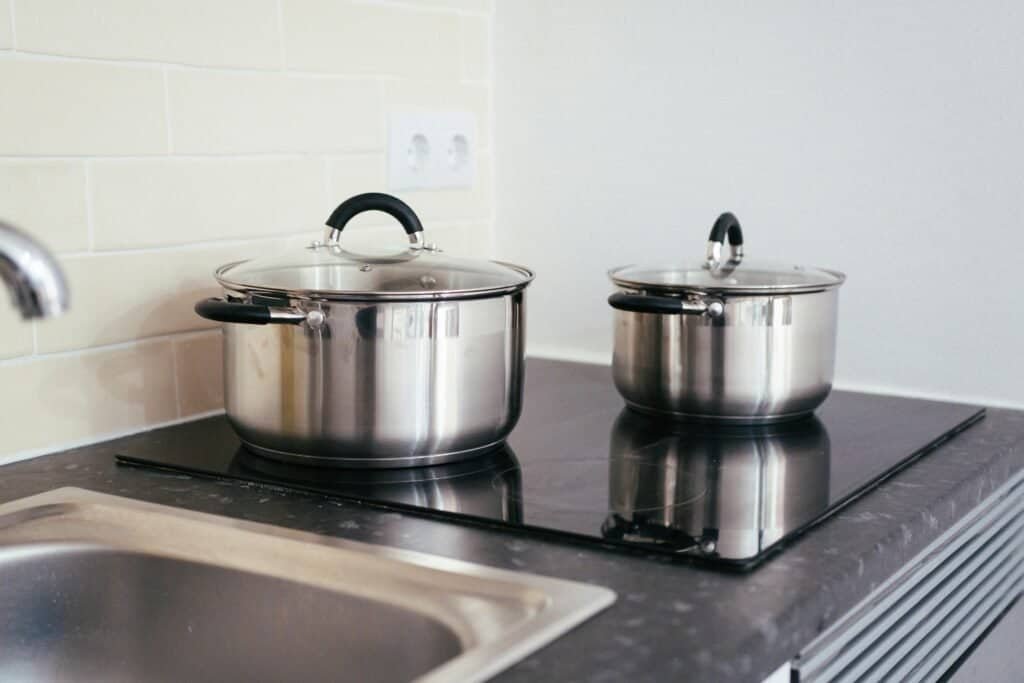 Stainless steel pots on a sleek black induction cooktop in a minimalist kitchen setting.