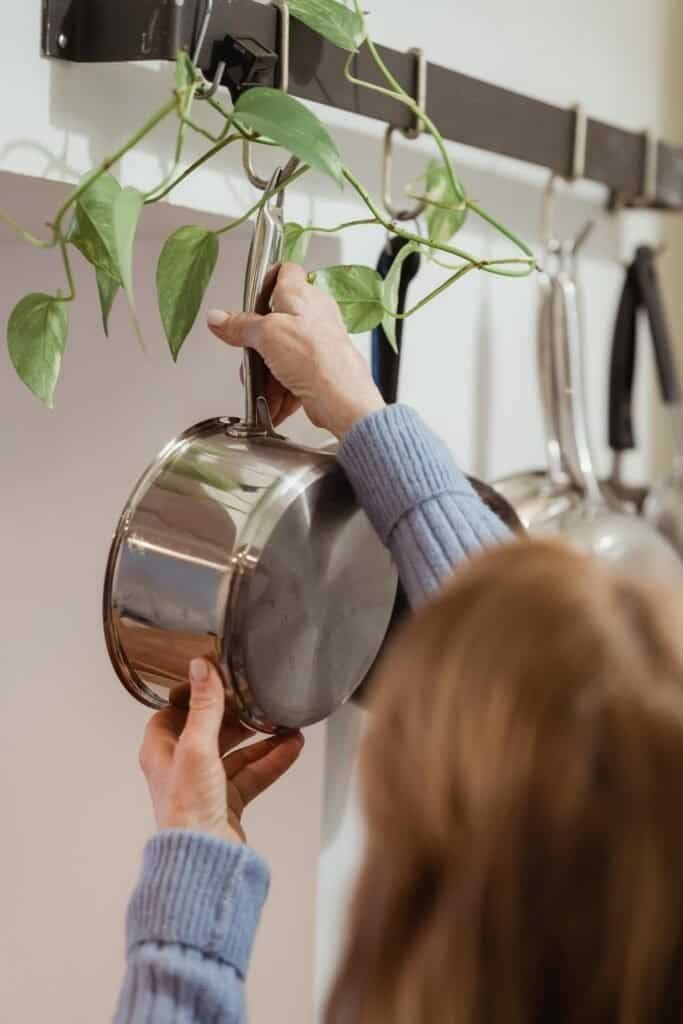 Person hanging a stainless steel pot on a wall-mounted rack in a tidy kitchen.