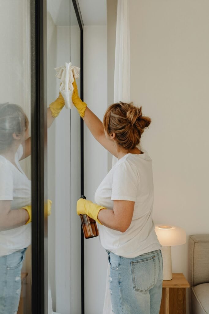 Woman cleaning glass mirror with cloth and spray in modern home.
