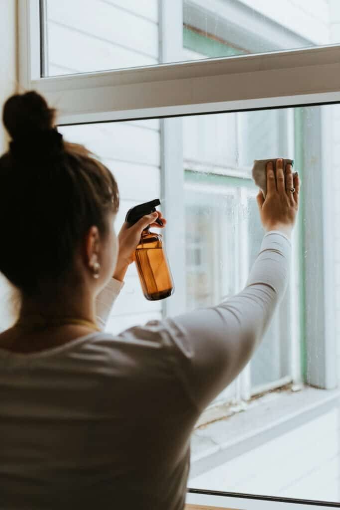 Woman cleaning window with spray bottle and cloth, home window cleaning, eco-friendly cleaning.
