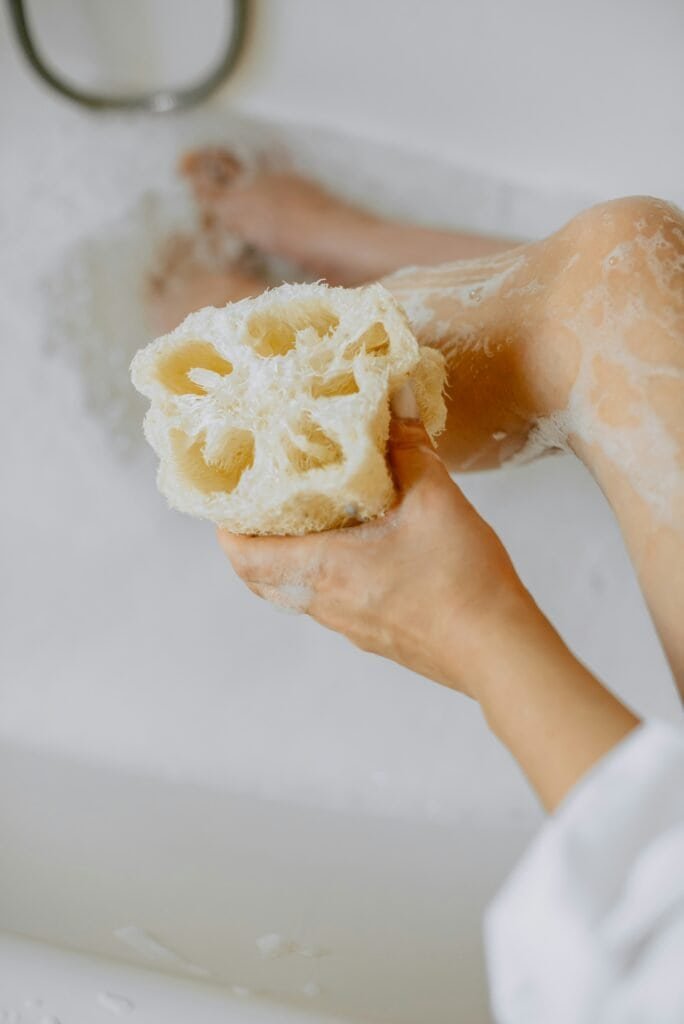 Person using natural loofah sponge for gentle body exfoliation.