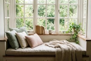 Reading nook ideas: charming cottage window seat with sage and blush pillows, knit throw, and garden view